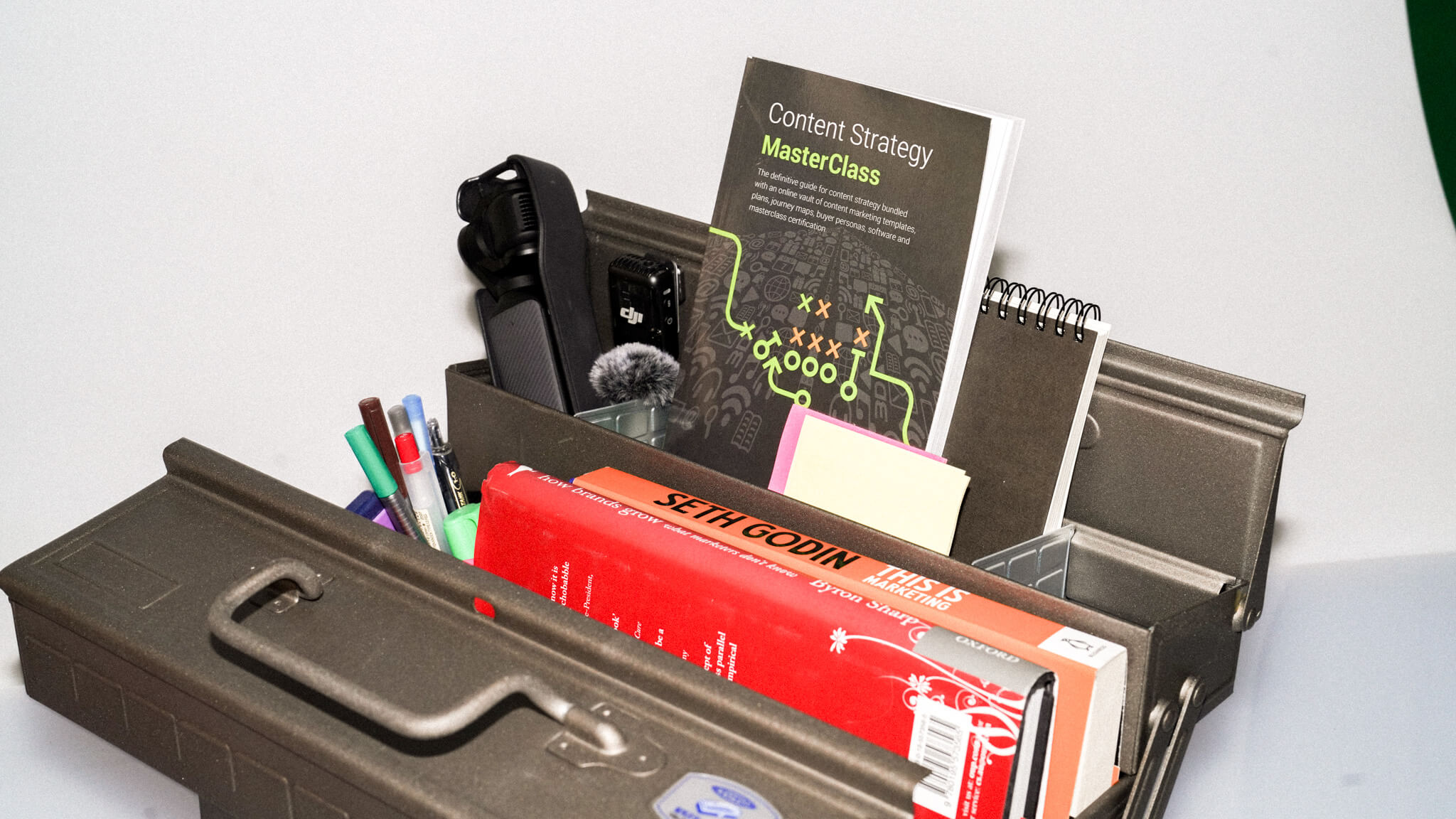 A black desk organiser containing office supplies, markers, and books including 'Content Strategy Masterclass' and other marketing materials.