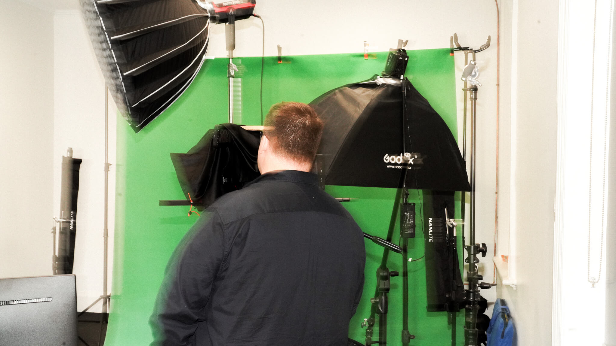 Videographer adjusting studio lights in front of green screen backdrop with professional equipment.