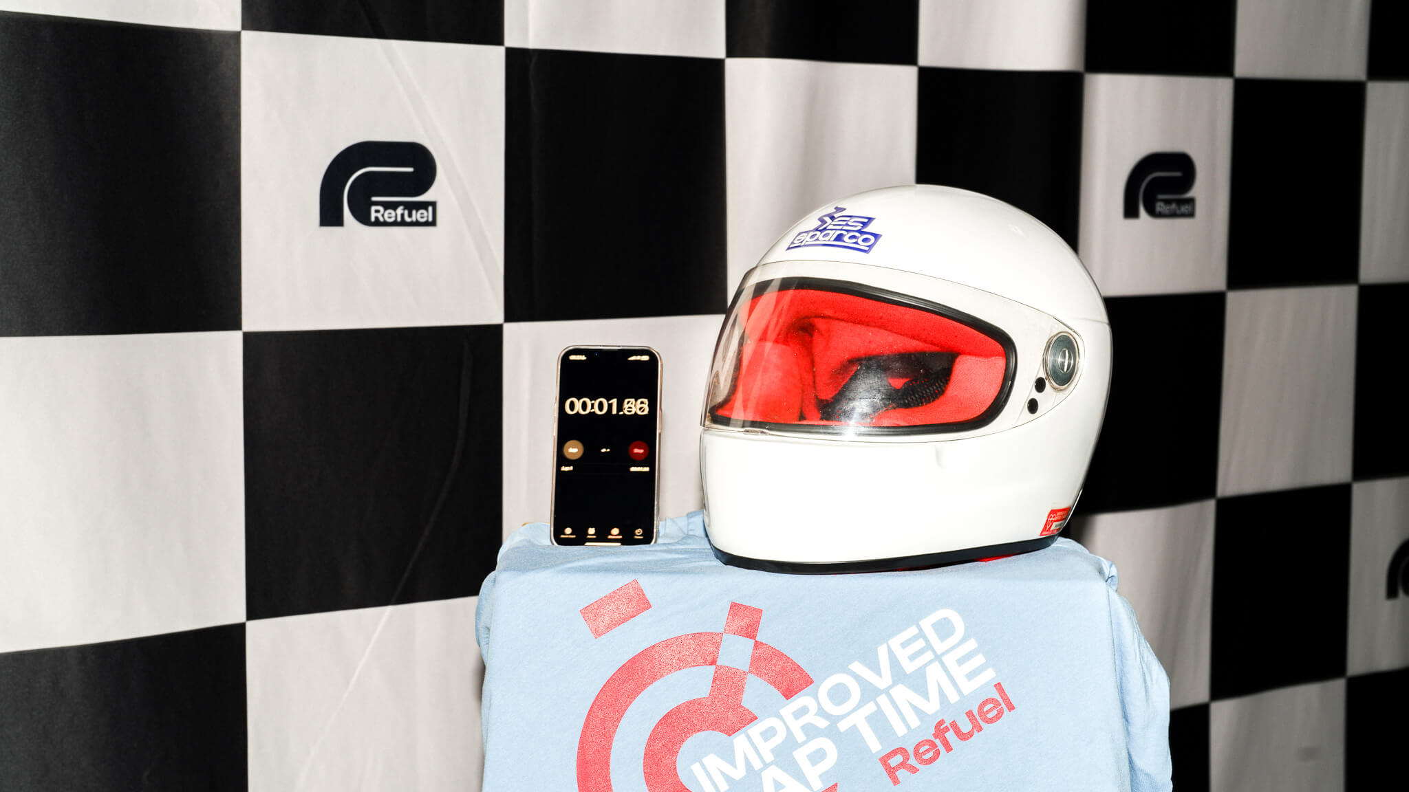 White racing helmet with red visor and phone showing timer on checkered flag backdrop with Refuel branding.