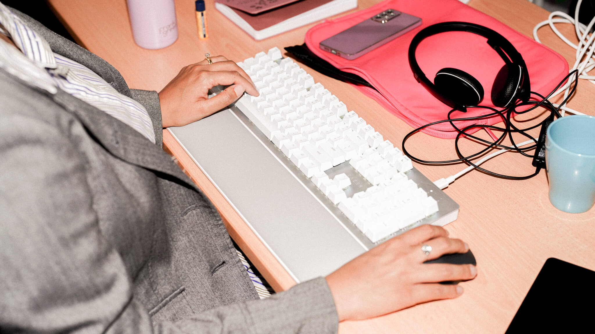 Hands typing on a Logitech keyboard next to a laptop, with marketing textbooks including 'Conversational Marketing' stacked on the wooden desk.