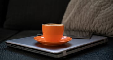 Orange coffee cup on laptop sitting on couch