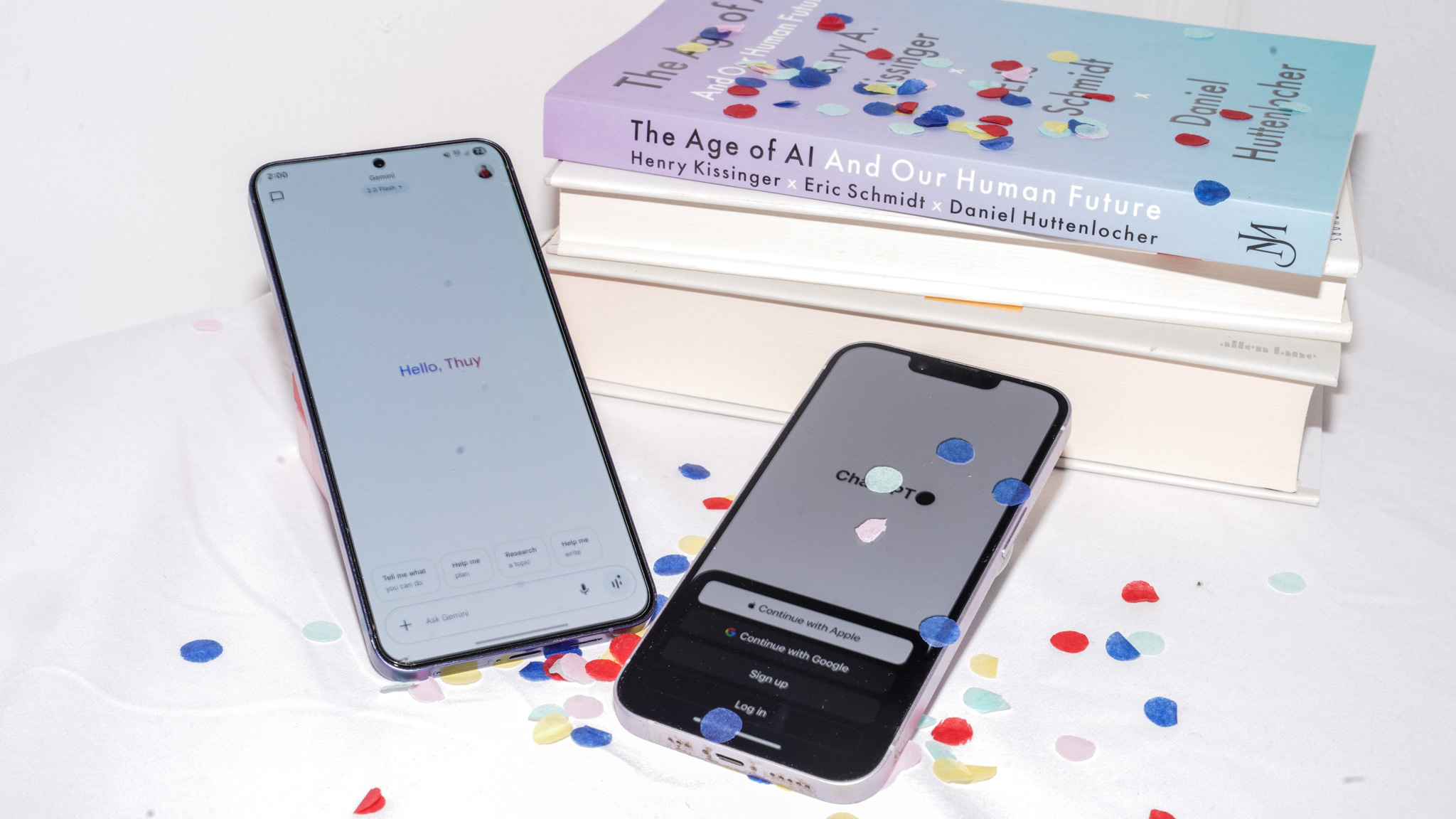 Two smartphones with AI apps beside "The Age of AI" book with confetti.