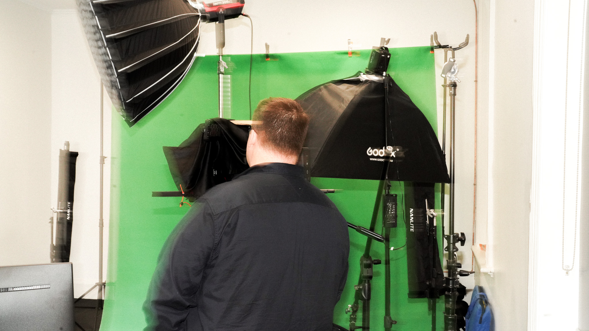 Videographer adjusting studio lights in front of green screen backdrop with professional equipment.