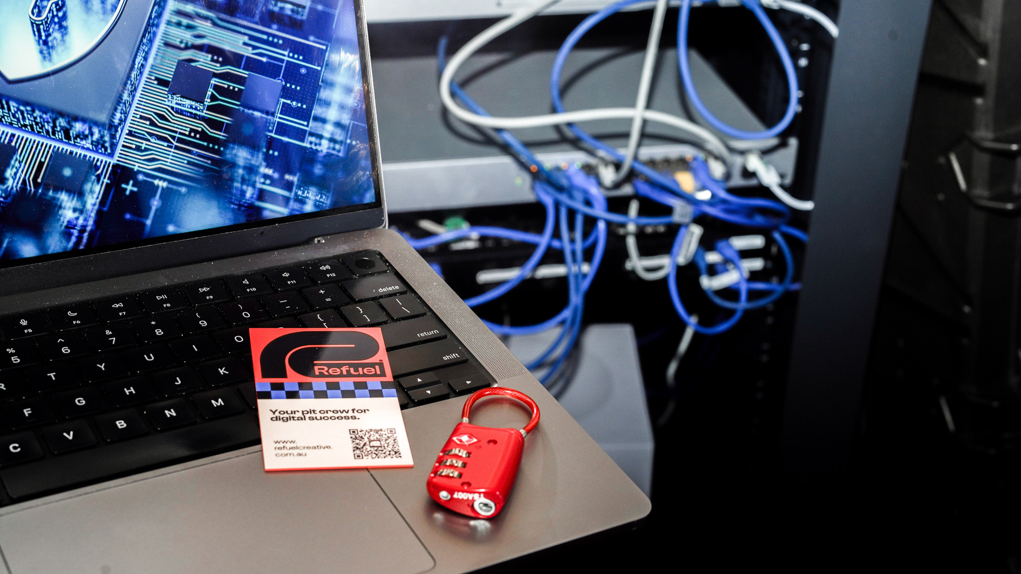 Red lock on laptop next to a Refuel Creative business card and network cables in tech workspace.