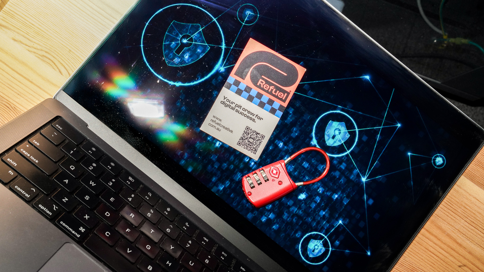 Laptop displaying futuristic network interface with red lock and Refuel business card on screen.