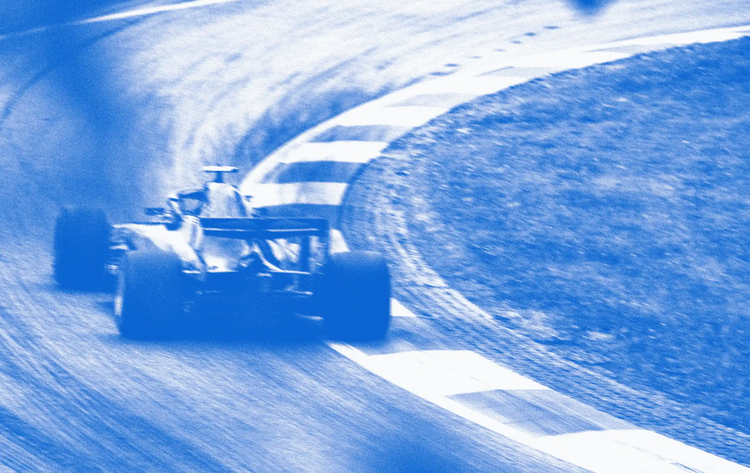 A stylized, blue-toned, and motion-blurred image of a Formula 1 race car speeding around a corner on a racetrack, seen from a rear-three-quarter view.