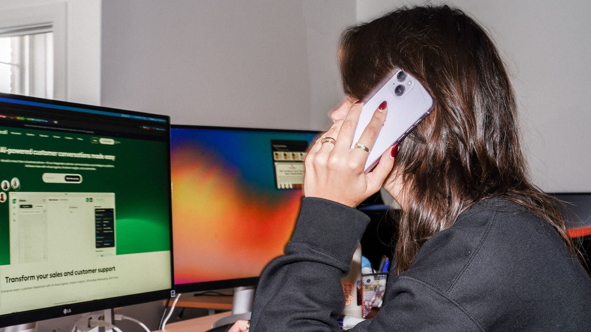 Employee using phone system while working at computer workstation with multiple monitors